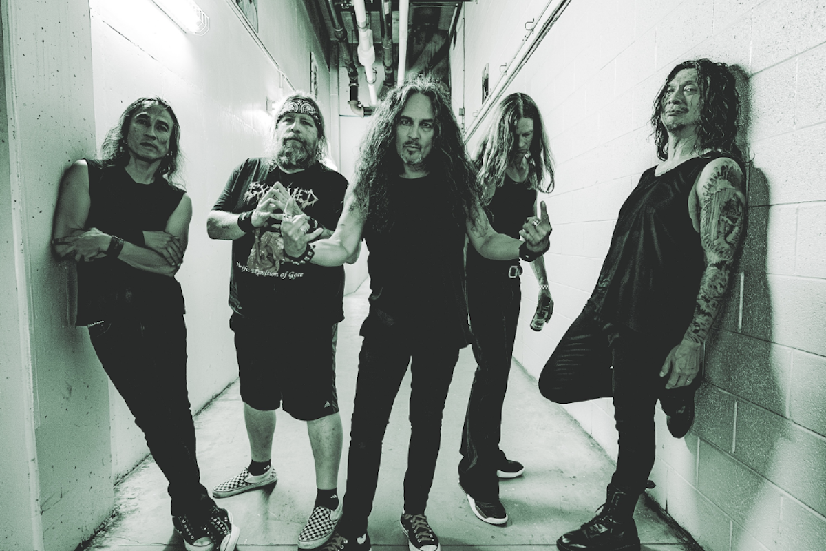 Thrash metal band Death Angel posing in a narrow concrete hallway wearing black outfits in a monochrome portrait.